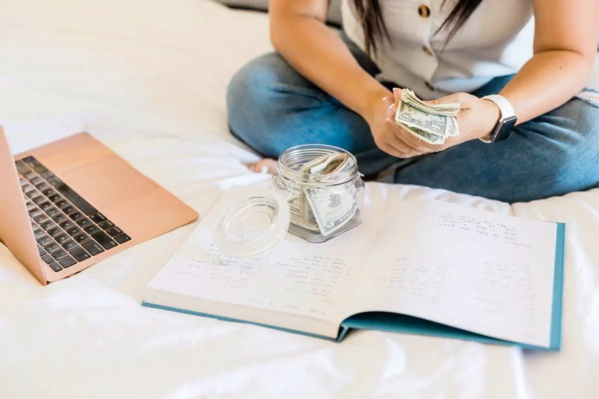 woman with cash, notebook, and laptop on bed