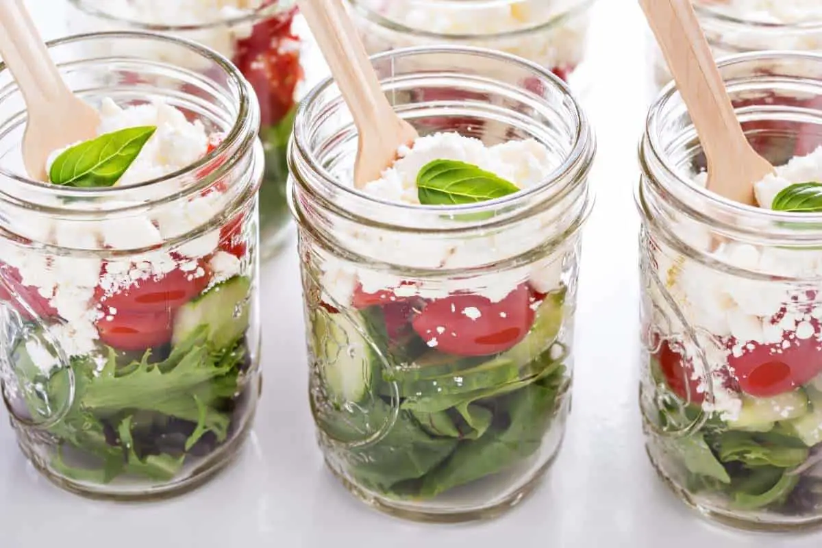 3 glass jars layered with lettuce tomato and feta cheese