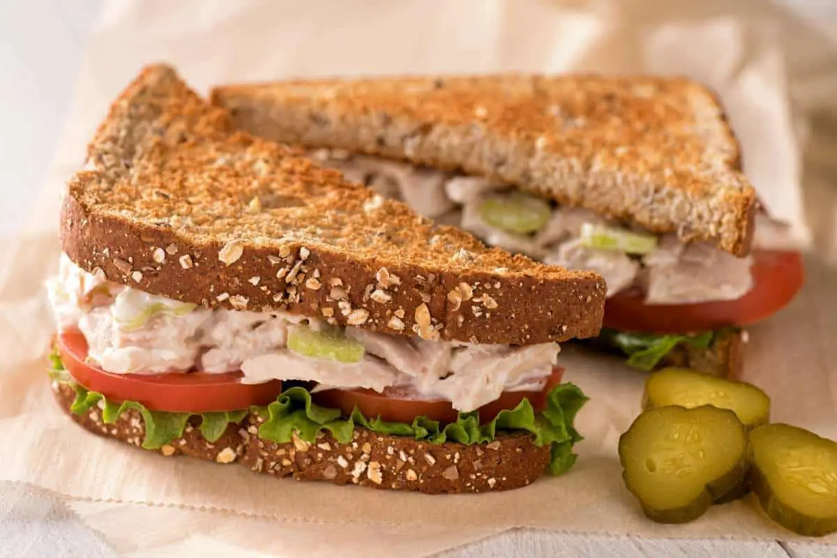 tuna sandwich on whole wheat bread with pickles on the side